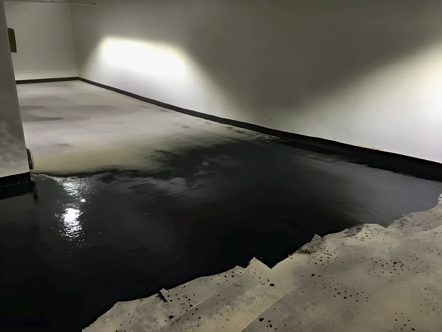 Black coat of the Kelmar system spread across the prepared slab at 980 Howe Street, carried to the wall as a black cove