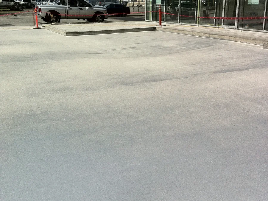 Aggregate broadcast across an exterior parkade deck in Abbotsford, the fresh smooth coat still showing in the foreground