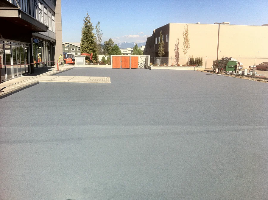 Finished grey traffic coating across the exterior parkade deck of a strata building in Abbotsford, from the storefront walkway to the planters