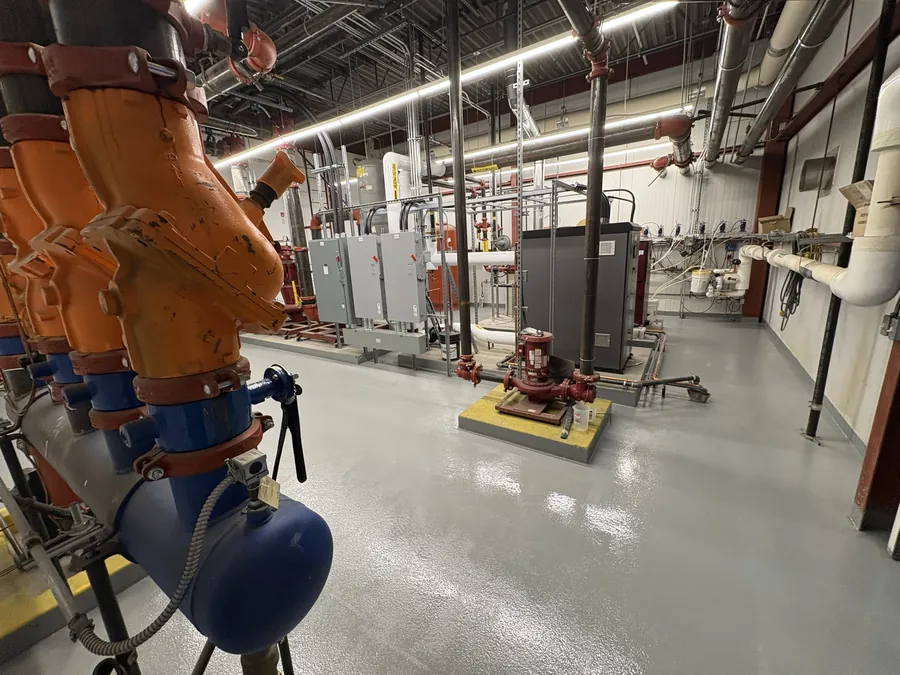Finished grey broadcast-textured traffic coating across a Canadian Tire mechanical room floor, between pump plinths and switchgear