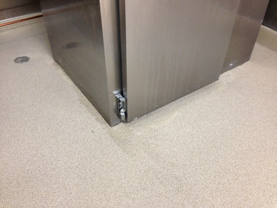 Decorative quartz floor laid tight around the base of stainless equipment beside a floor drain at Costco, Abbotsford