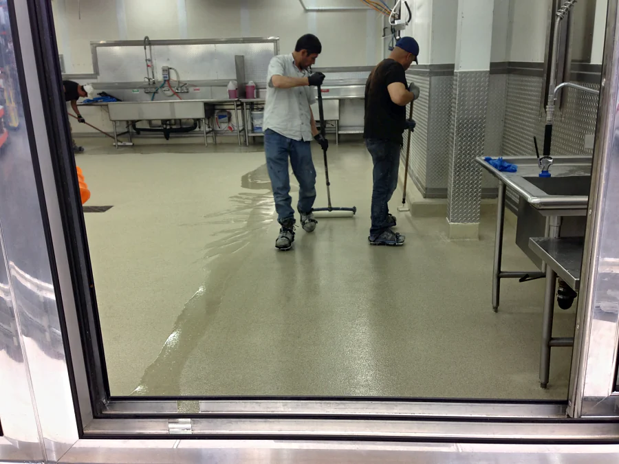 The crew spreading the floor past the sinks at Costco Abbotsford, seen through a doorway