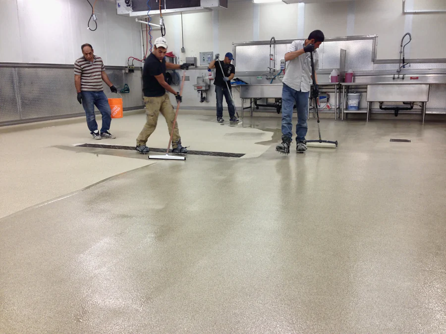 Crew spreading the decorative quartz floor with squeegees across the Costco prep room in Abbotsford, past the trench drain