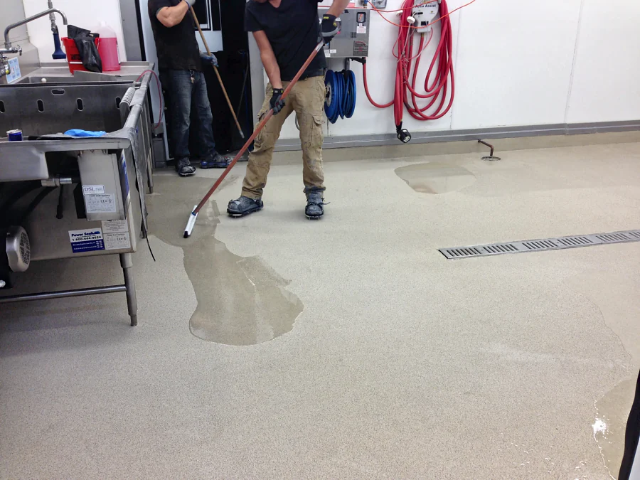 Installer squeegeeing the decorative quartz floor past the sinks and a trench drain in the Costco prep room, Abbotsford