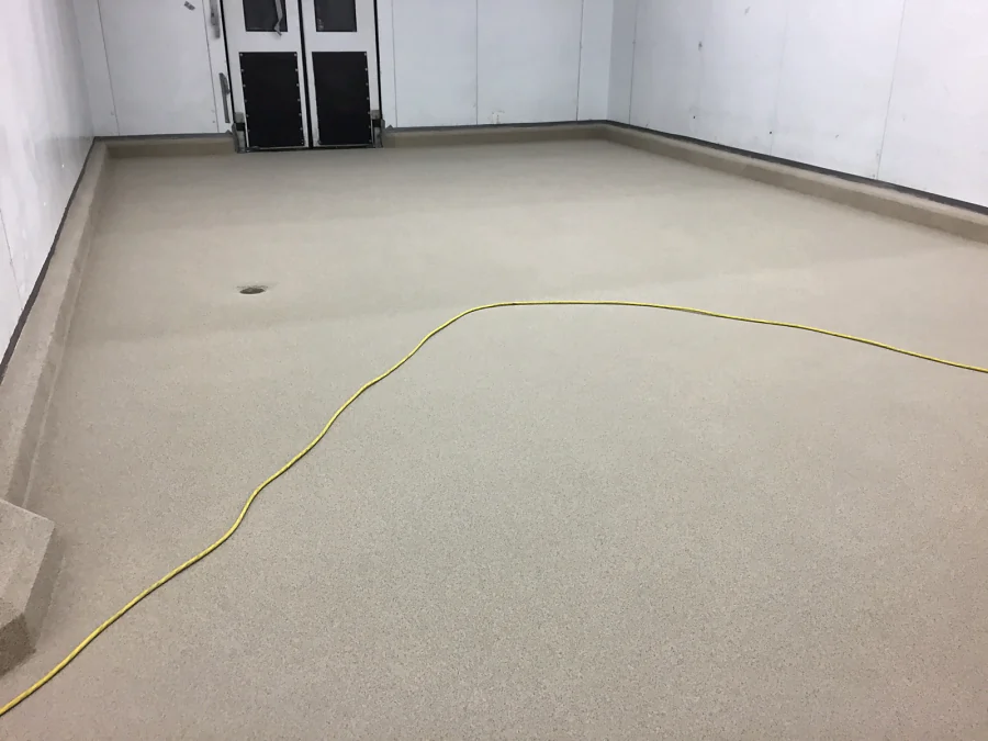 Finished decorative quartz floor through a white-panelled back-of-house room at Costco Kamloops, coved at every wall, with a floor drain