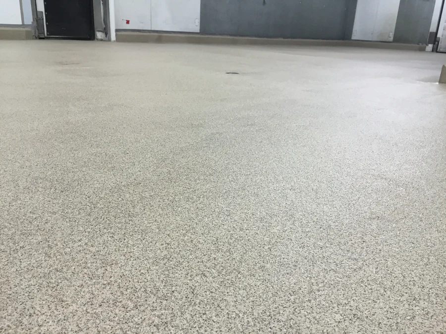 Close view of the finished decorative quartz floor at Costco Prince George, the tan and grey grains running back to a floor drain and the coved base