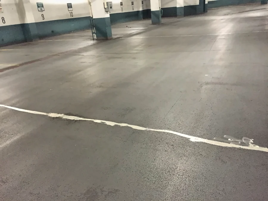 A crack filled across the drive aisle of a Downtown Vancouver parkade before the traffic coating, the stall numbers on the teal-banded walls beyond