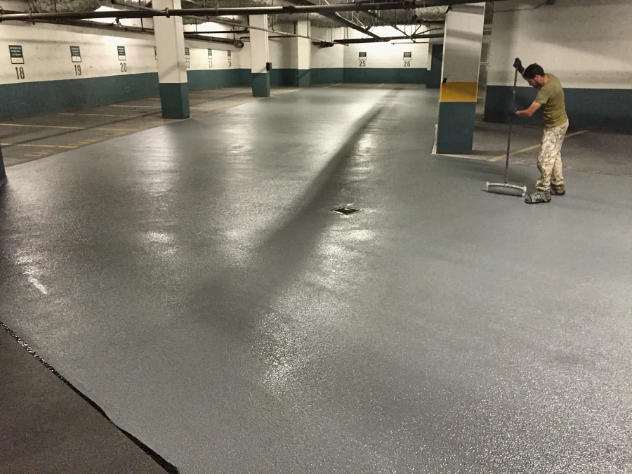 A crew member rolling out the grey traffic coating down the drive aisle of an underground parkade in Downtown Vancouver, past the numbered stalls