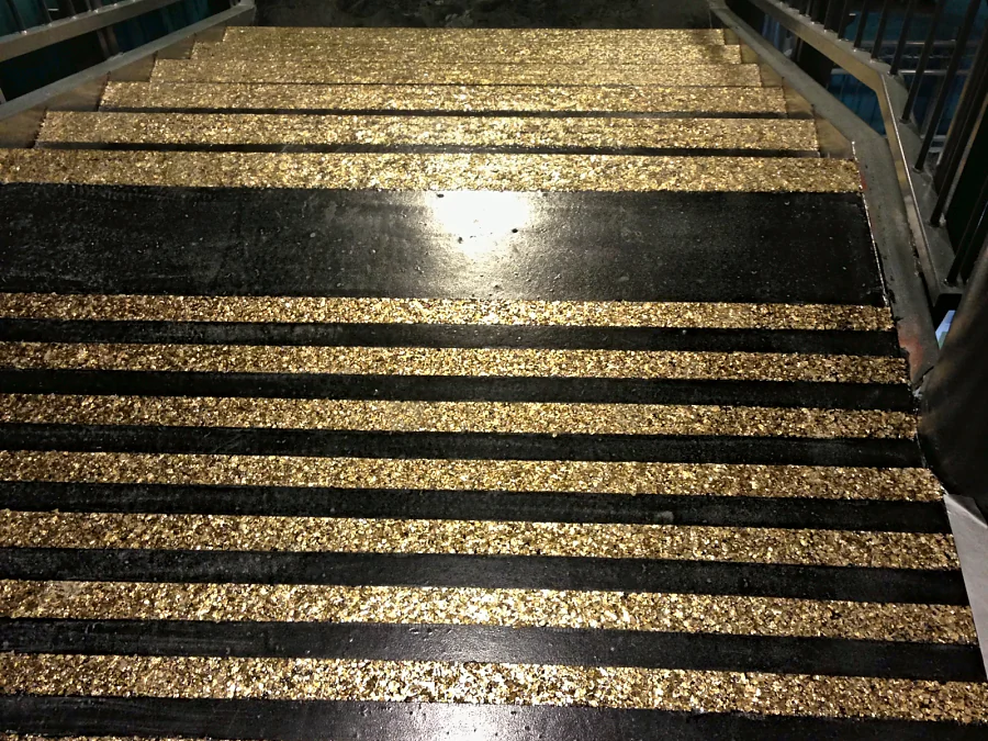 A stair landing at Hard Rock Casino Coquitlam in black with bands of gold flake warning strips, the gold stair nosings beyond