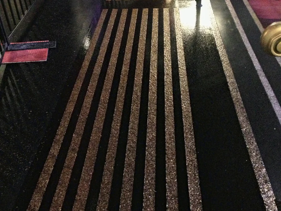 Gold flake warning strips running the length of a black walkway at Hard Rock Casino Coquitlam, beside the casino carpet