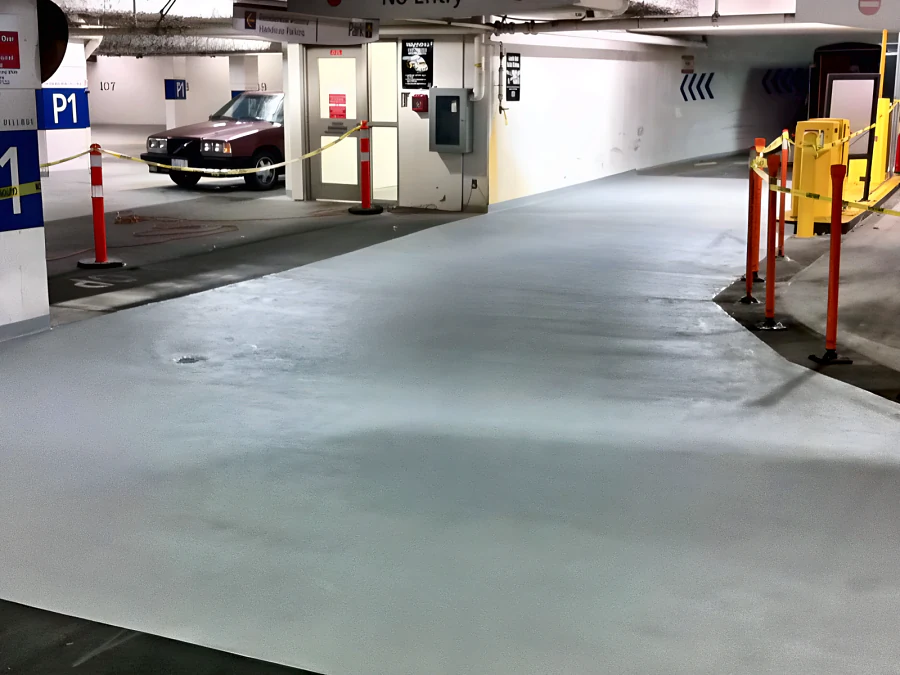 Freshly resurfaced grey drive aisle and ramp approach at the International Village parkade in Vancouver, with P1 signage and barrier posts