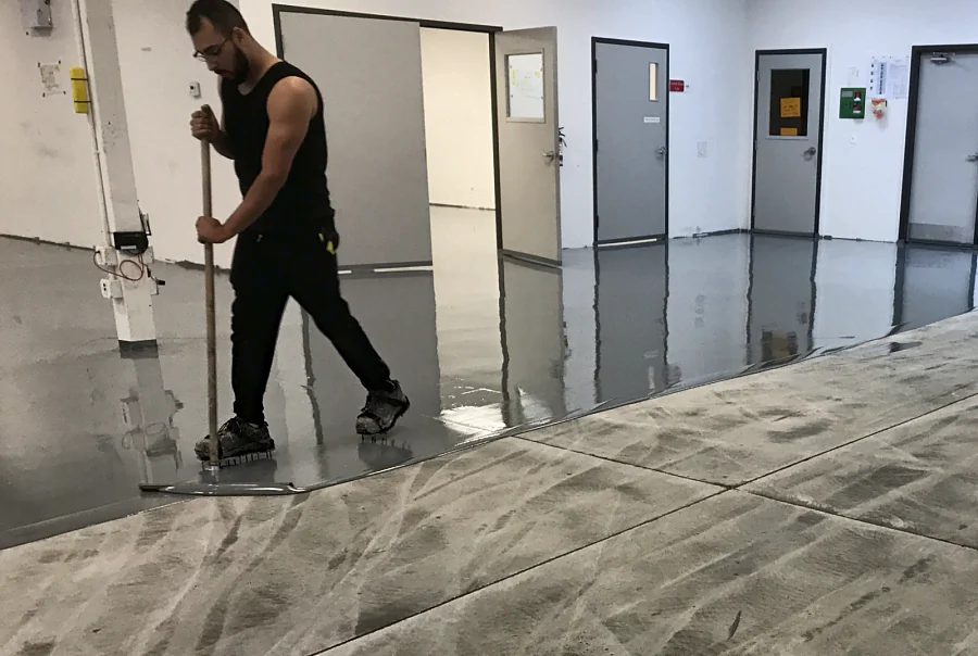 A crew member spreading the grey ESD floor coating by squeegee over the ground slab of a Kodak-owned printing company in Richmond