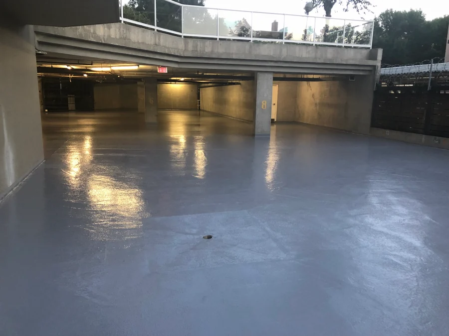 The finished level at dusk, the coat with its sheen past the drain to the open end of the parkade
