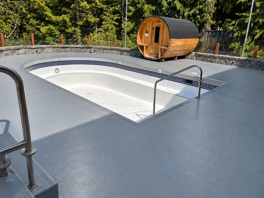 The grey ResinTech EWS deck round the pool at Nita Lake Lodge, out to the stone wall and the cedar barrel sauna