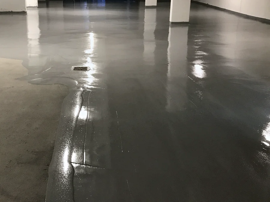 The grey traffic coating flowing out over the bare concrete slab and round the floor drain in a North Vancouver residential parkade