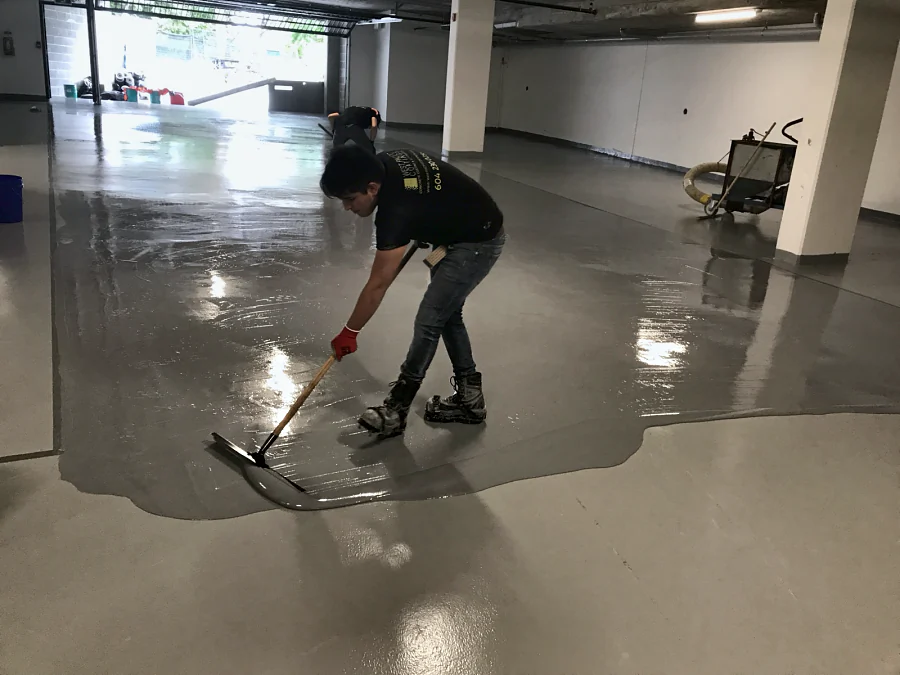 A crew member spreading the grey Tremco Vulkem 350NF/950NF/950NF coat by squeegee across a residential parkade in North Vancouver for Milori Homes