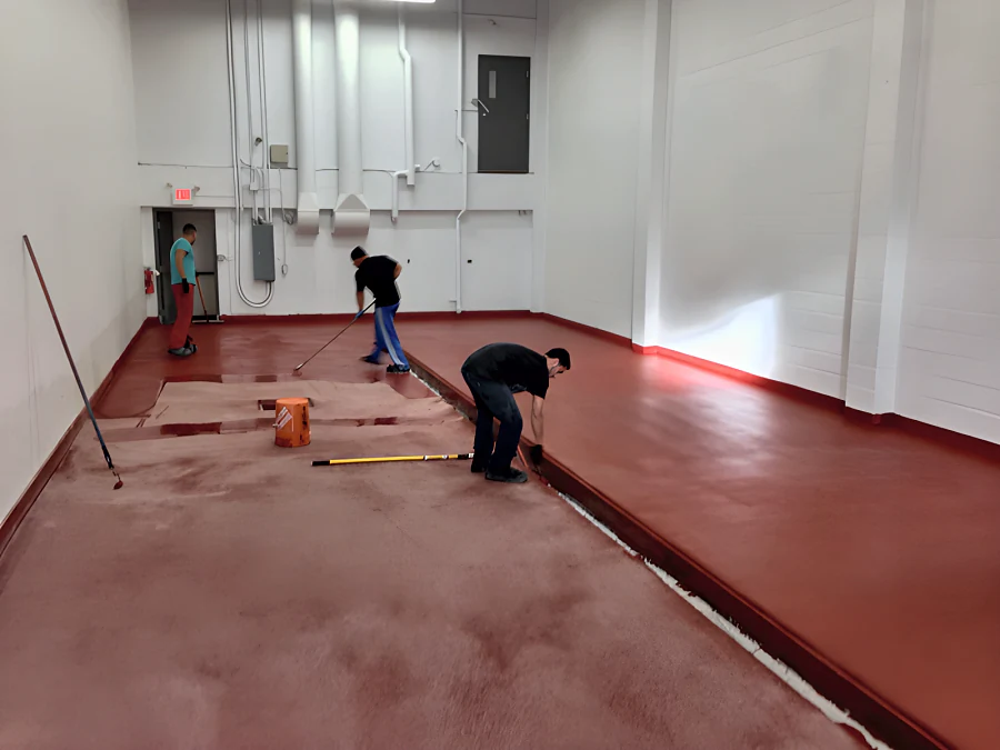 Crew laying the red EWS floor in phase 2 at Parallel 49 Brewing Company, Vancouver, with aggregate broadcast into the wet coat beside the trench drain