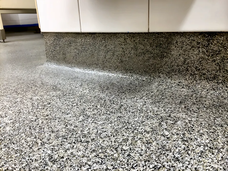 The coved junction where the decorative quartz floor turns up under the tiled wall in a Surrey school washroom