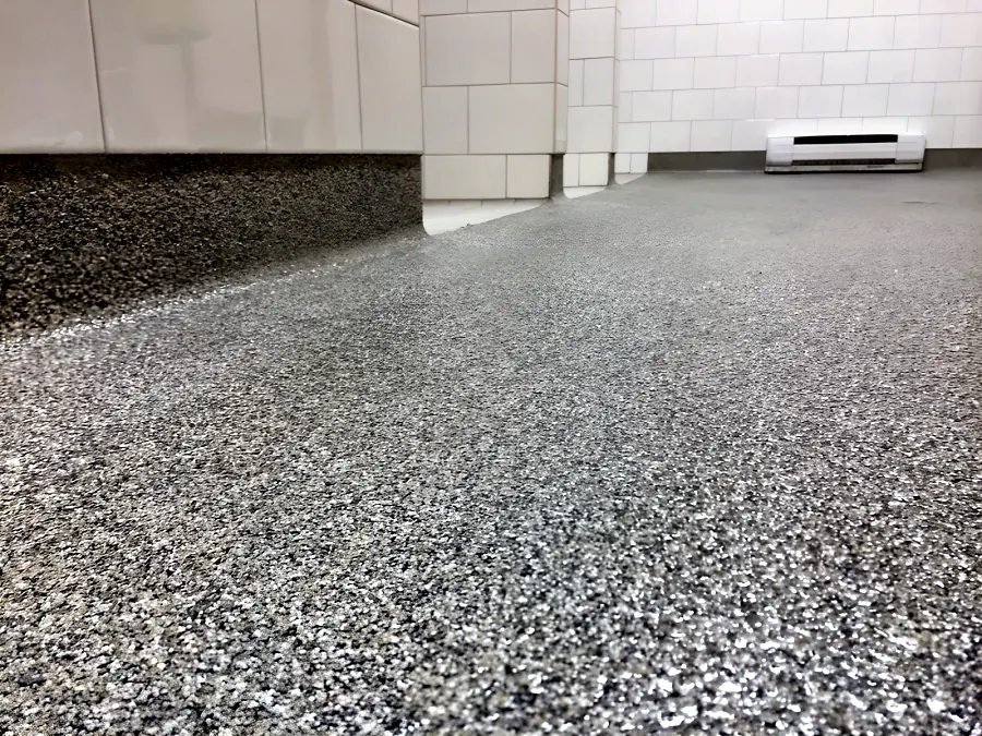Decorative quartz floor in a Surrey school washroom, carried up the base of the tiled plinth as a coved skirting