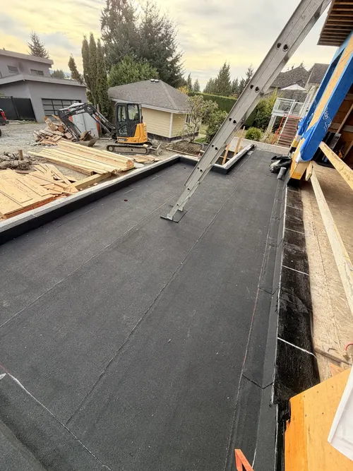 Torch-on cap sheet across a flat roof area of a new house, the laps staggered and the membrane turned up and over the curbs