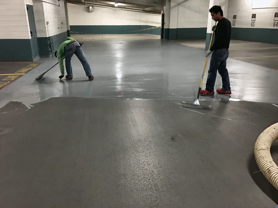 A top coat going down by squeegee and roller over a shot-blasted parkade drive aisle in a Vancouver residential building, 2016