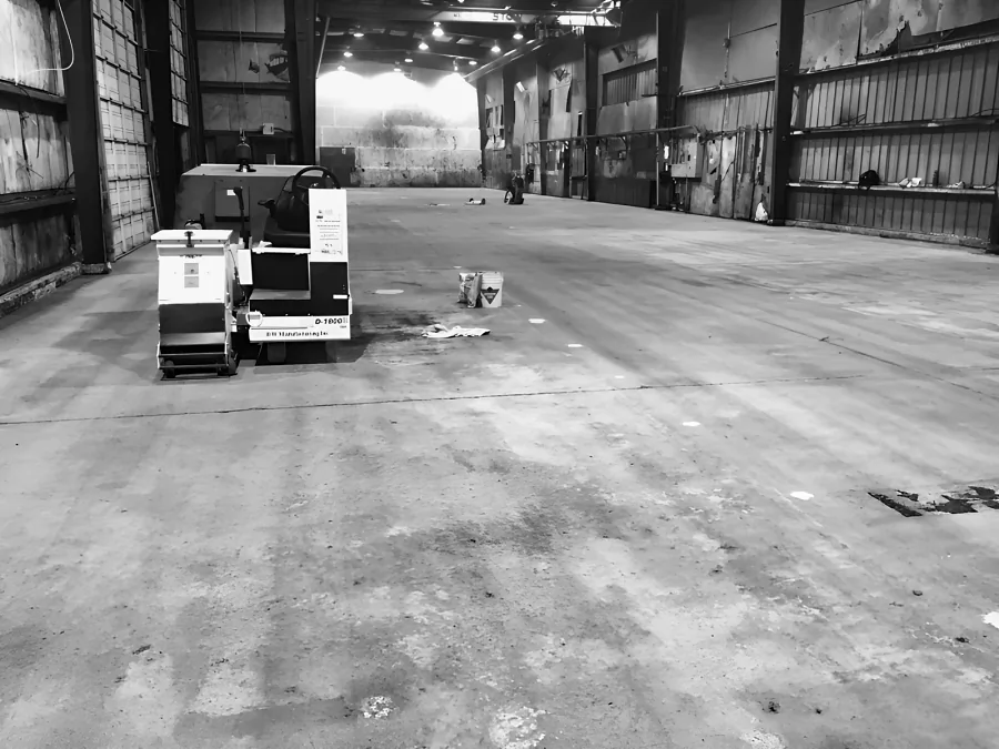 Ride-on shot blaster in a long industrial warehouse, the slab being blasted and cleaned before the epoxy and urethane went down