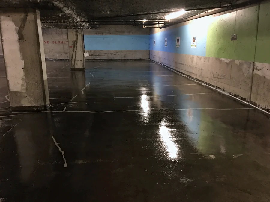 A dark first coat over the prepared slab of a residential parkade on West Broadway, Vancouver, the treated cracks showing through