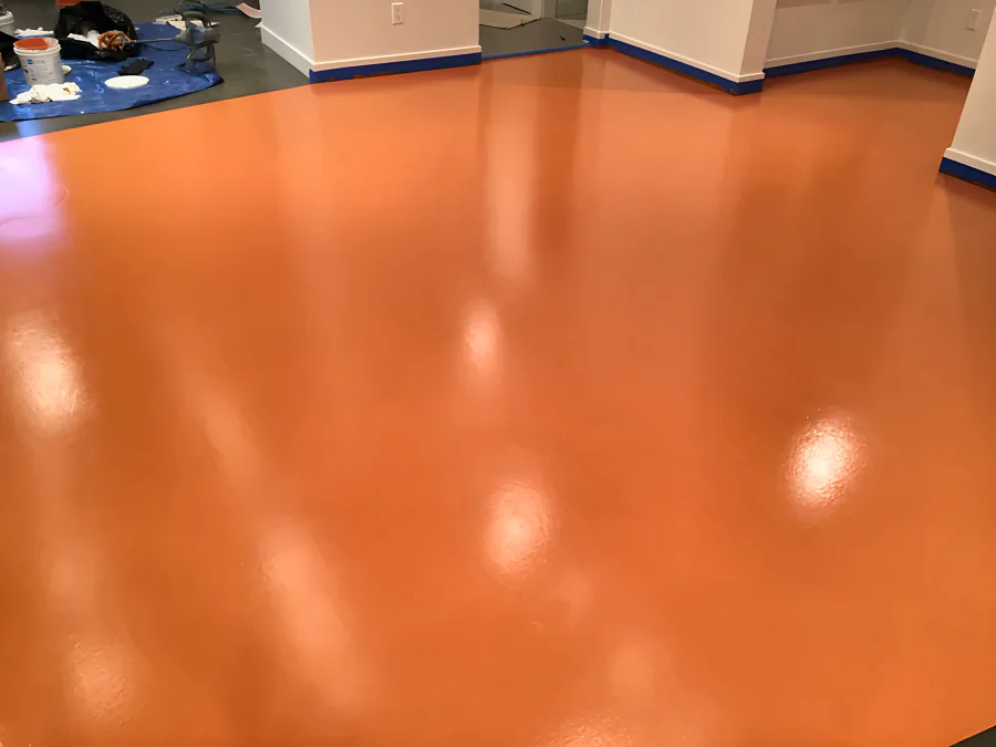 High-gloss pumpkin-orange urethane floor across an open room in Whistler, the walls masked with blue tape